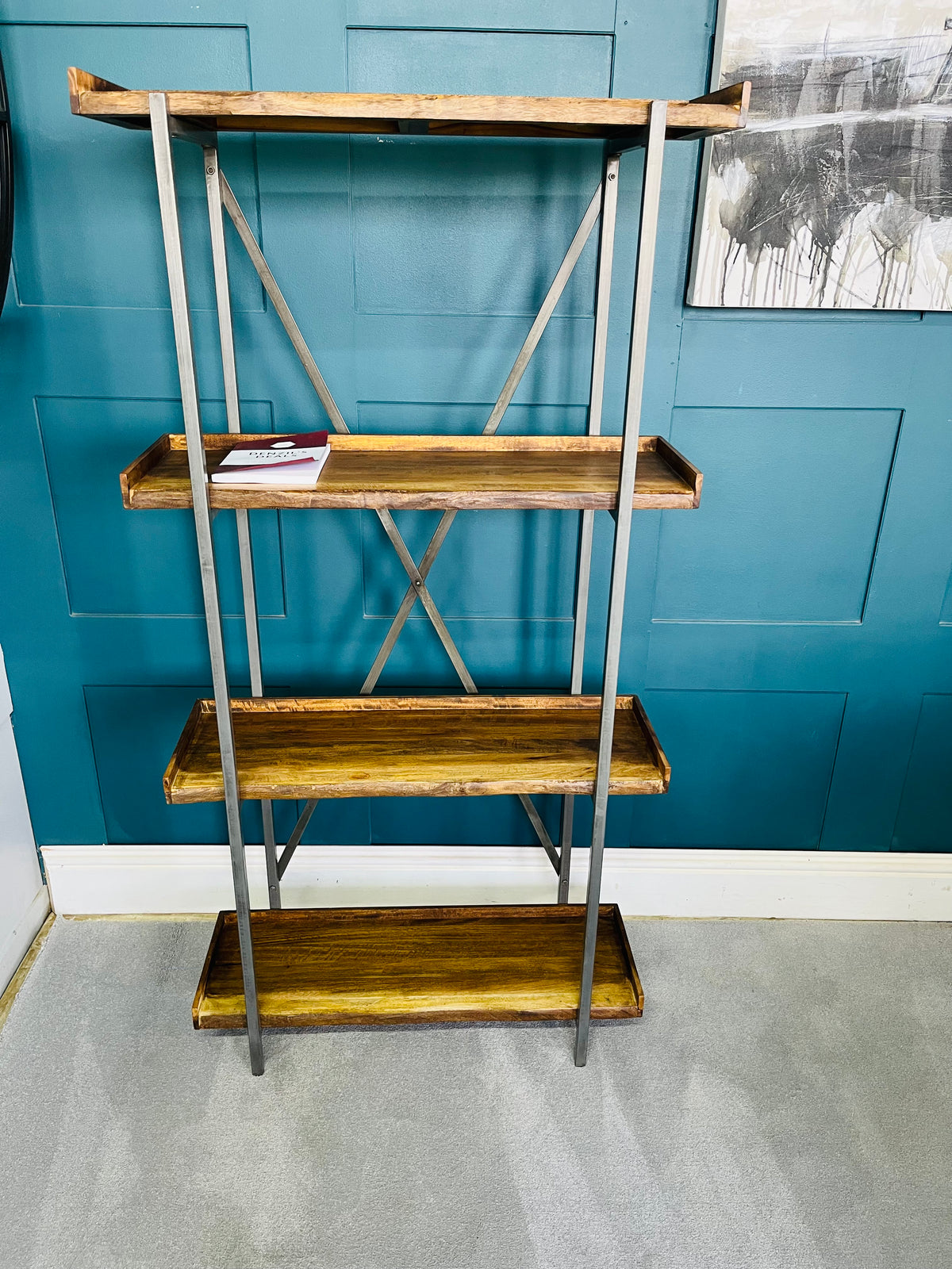 Modern minimalist oak shelving unit with four staggered, asymmetric shelves. The natural wood grain and live-edge detailing contrast against a clean geometric layout, styled with books and ornaments inside a contemporary living room