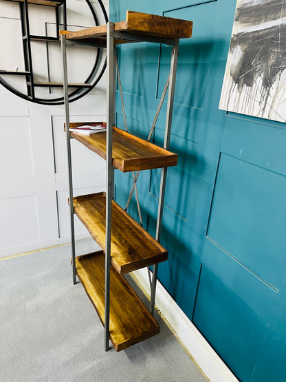 Modern minimalist oak shelving unit with four staggered, asymmetric shelves. The natural wood grain and live-edge detailing contrast against a clean geometric layout, styled with books and ornaments inside a contemporary living room