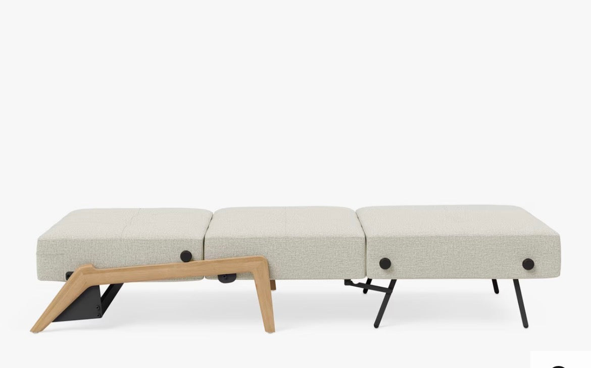 Modern single armchair bed by Innovation Living, shown in Mixed Dance Natural light cream-beige marled fabric. The chair has a square, blocky design with a thick seat cushion, a flat backrest, and low-profile light wood legs. It features a space-saving design that folds out seamlessly into a single bed.