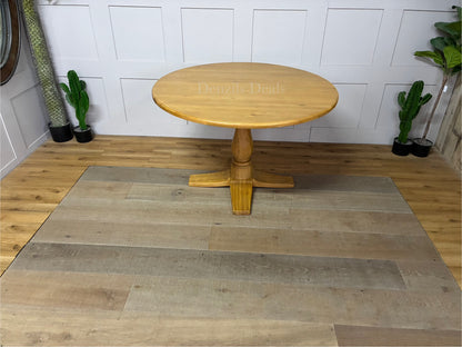 Oak Furnitureland Henley range round dining table in natural oak. The image features a solid hardwood circular top with visible wood grains, supported by an ornate, chunky carved central pedestal column base resting on a stable cross-shaped foot