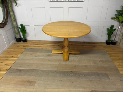Oak Furnitureland Henley range round dining table in natural oak. The image features a solid hardwood circular top with visible wood grains, supported by an ornate, chunky carved central pedestal column base resting on a stable cross-shaped foot