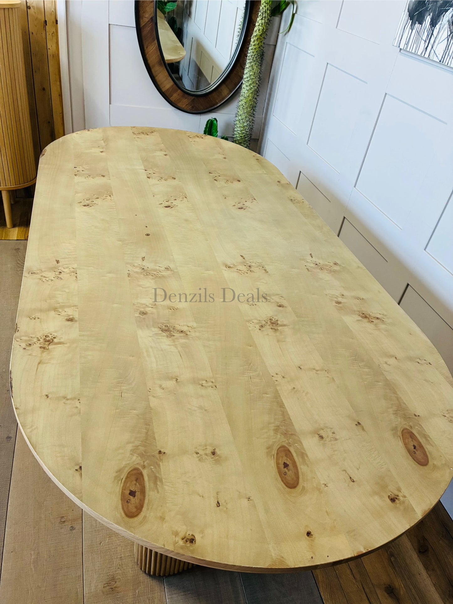 A wide, oval dining table by Anthropologie with a rich burled veneer tabletop and a sculptural, fluted ash wood base