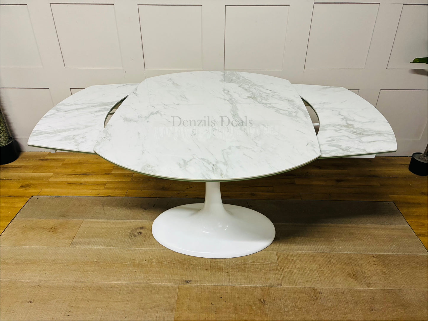 Round extending dining table from DFS featuring a white ceramic marble-effect top, curved edges, and a matching white fibreglass tulip base. Shown in a modern dining room setting."