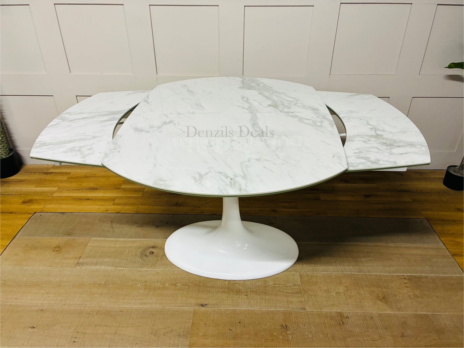 Round extending dining table from DFS featuring a white ceramic marble-effect top, curved edges, and a matching white fibreglass tulip base. Shown in a modern dining room setting."