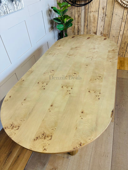 A wide, rounded dining table by Anthropologie with a rich burled veneer tabletop and a sculptural, fluted ash wood base