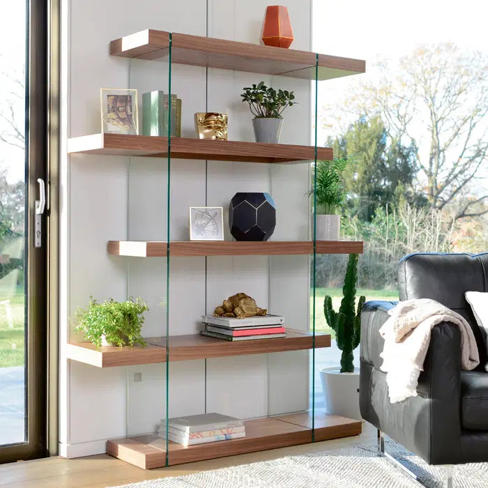 Dwell Sturado shelving unit styled in a modern living room, loaded with decorative vases, hardcover books, and potted plants."