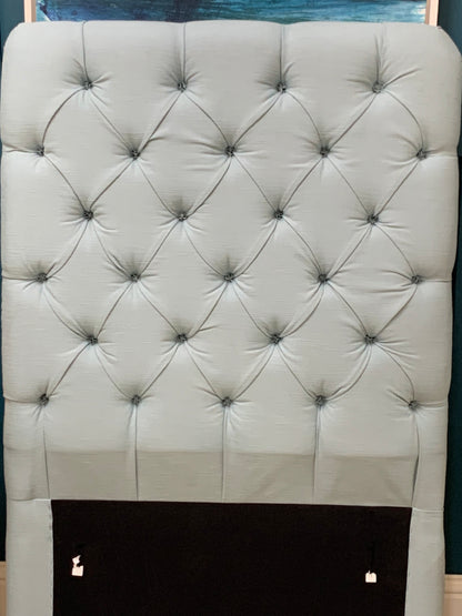 Tall Loaf single headboard upholstered in light blue cotton-linen fabric. It features a soft, generously padded, rectangular shape with laid-back, curved edges and a French seam