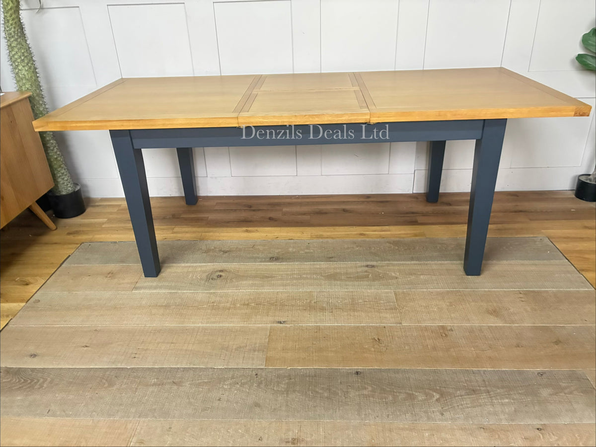 The maud-navy Extending Dining Table from DFS features a navy-finished acacia frame and legs with a solid oak frame and veneer tabletop showing natural wood grain