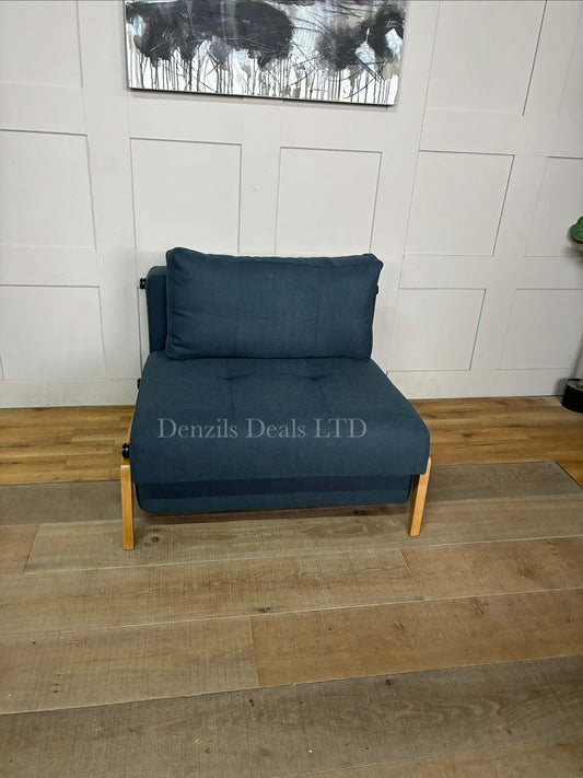 The Innovation Living Cubed 90 Armchair Bed in Nist Blue 515 is a compact, Scandinavian-designed single chair bed priced around £1,199. It features an automatic leg-folding conversion mechanism, a No-zag spring mattress, and a hidden storage box in the seat