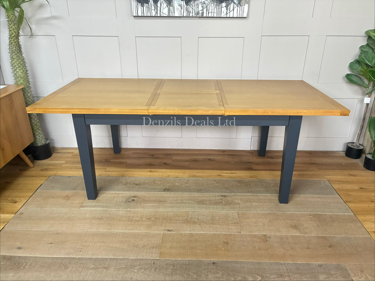 The maud-navy Extending Dining Table from DFS features a navy-finished acacia frame and legs with a solid oak frame and veneer tabletop showing natural wood grain