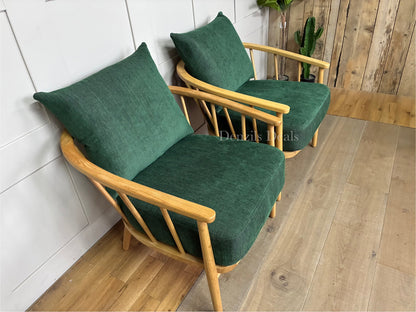 Two mid-century style John Lewis Frome armchairs side by side, featuring rich forest green fabric, plush foam cushions, and a curved silhouette cradled by a light natural oak frame.