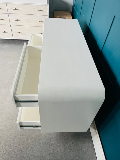 Modern low-slung white lacquered dresser with rounded edges and cylindrical block feet.