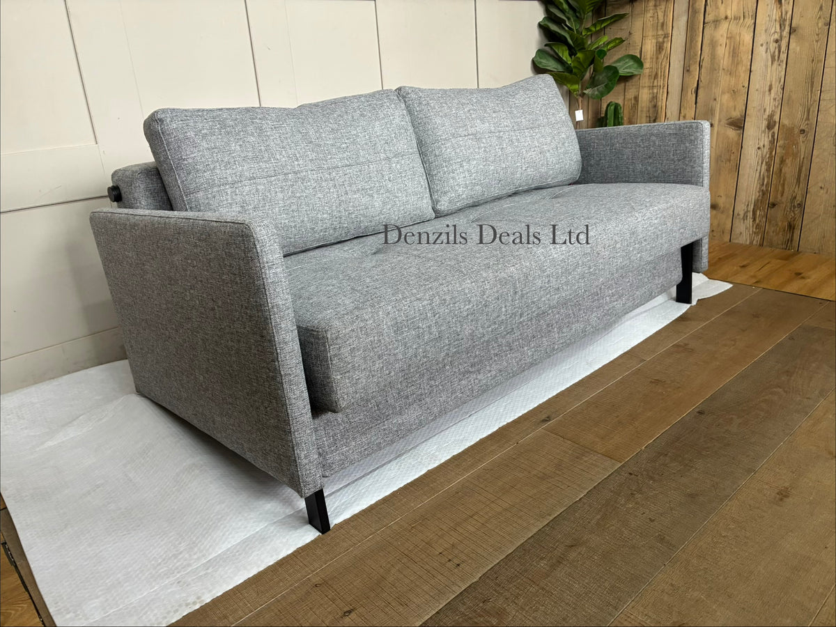 A contemporary living room featuring the compact Innovation Living Cubed 160 Sofa Bed. The sleek, armless frame is covered in a durable Twist Granite grey fabric and elevated by slim black legs, styled with two rectangular plush back cushions.