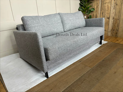 A contemporary living room featuring the compact Innovation Living Cubed 160 Sofa Bed. The sleek, armless frame is covered in a durable Twist Granite grey fabric and elevated by slim black legs, styled with two rectangular plush back cushions.
