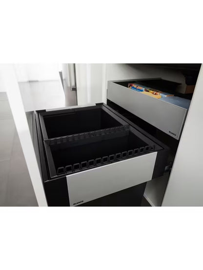 A BLANCO Select under-counter pull-out kitchen bin with two grey compartments, shown partially extended from a minimalist dark cabinet to reveal its 38-litre waste separation system. 