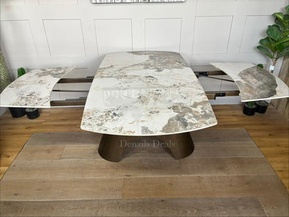 by a heavy-duty, sculptural metal pedestal base finished in a warm, matte bronze tone. The tabletop features a clean, seamless look with hidden internal tracking lines, illustrating its rotating extension mechanism that smoothly expands the surface from a compact six-seater to a larger eight-seater.