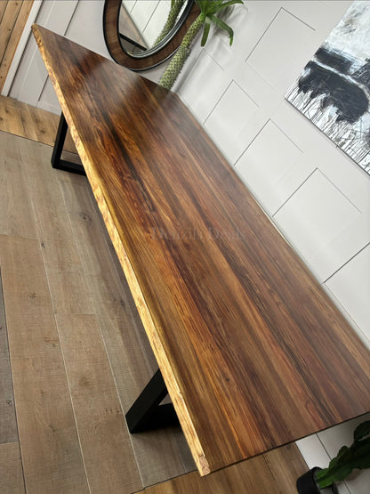 A modern industrial Bartolo dining table by Nick Scali. The rectangular table features a thick, warm-toned Tasmanian Blackwood tabletop with organic, wavy live edges that highlight the natural wood grain. The top rests on two heavy-duty, black powder-coated steel sleigh-style legs at either end, blending rustic warmth with a clean, industrial look