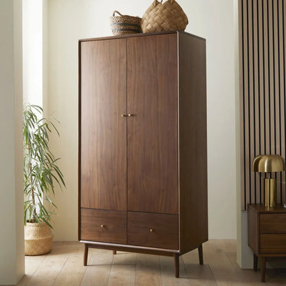 A mid-century modern two-door wooden wardrobe in a rich American walnut finish, featuring streamlined cabinet doors, polished brass knobs, and integrated base drawers